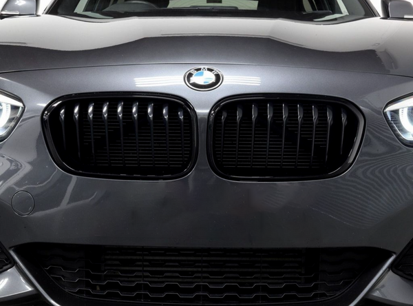Car grille with vertical slats, featuring a BMW logo above, is prominently displayed on a dark gray vehicle in a well-lit indoor setting.
