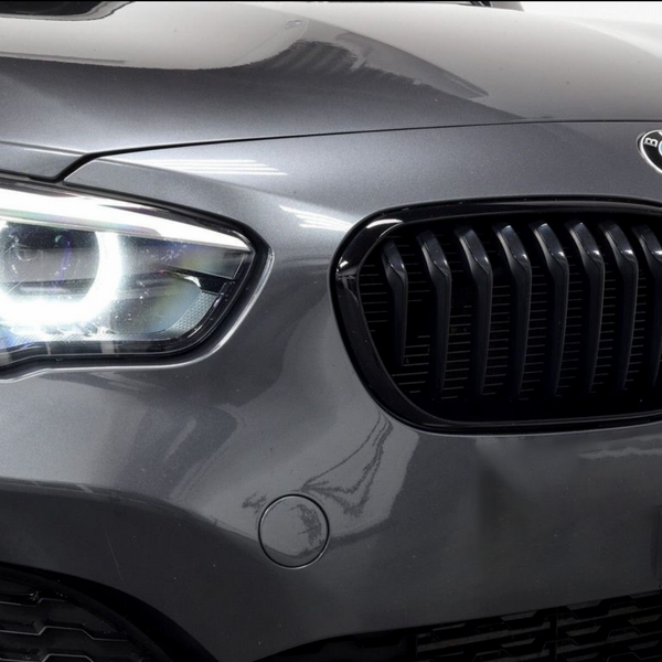 A car's front features illuminated headlights and a black kidney grille, with a BMW emblem on the hood, set in a glossy, grey exterior.