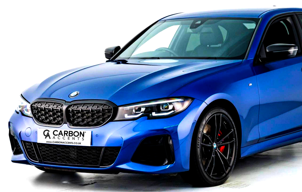 A blue car features a sleek design with black grille and alloy wheels. It is parked on a white background. The license plate reads: "CARBON ACCENTS www.carbonaccents.co.uk".