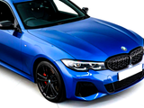 A metallic blue BMW car is stationary indoors, featuring a black grille, sporty headlights, and black wheels with red brake calipers. The environment is brightly lit, enhancing its sleek design.
