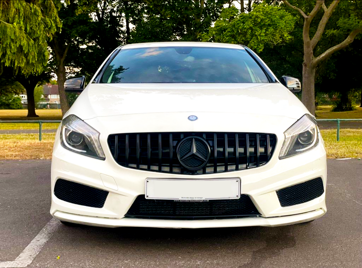 White car with a black grille and circular emblem, parked in an outdoor setting surrounded by lush green trees and a clear sky. License plate text: "Mercedes Benz of Ipswich www.mercedes-benzofipswich.co.uk".