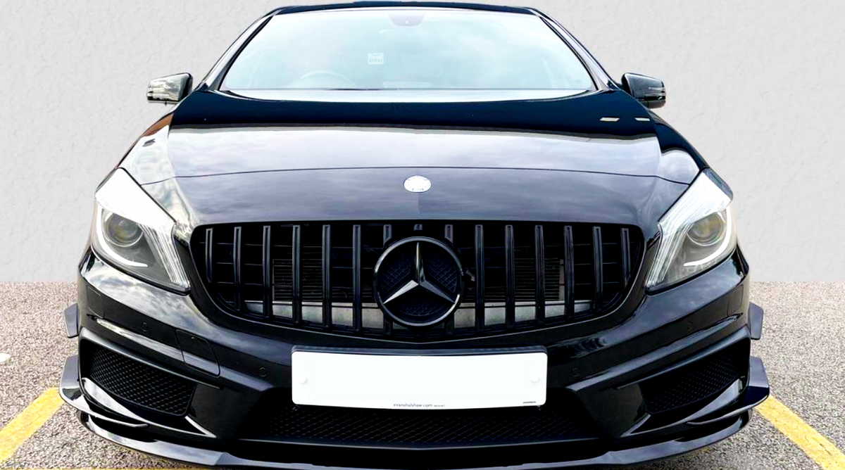 A black car with a prominent front grille features a Mercedes emblem, parked on an asphalt surface. License plate reads: "manahawkin.com service." Yellow parking lines mark the ground.