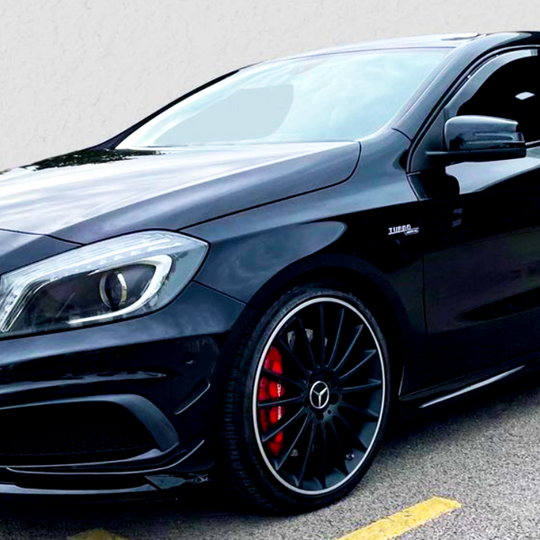 A sleek, black Mercedes-Benz hatchback with sporty, red brake calipers is parked on asphalt. It has a distinctive front grille and the emblem "Turbo 4MATIC" on the side.