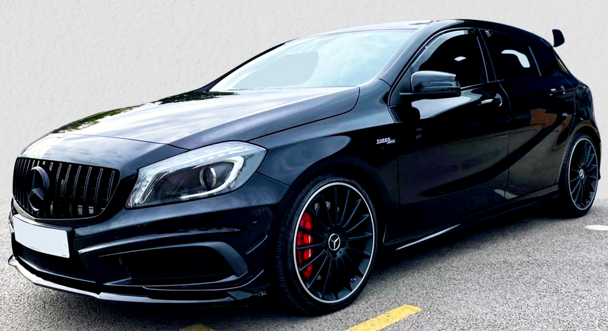 A sleek, black Mercedes-Benz hatchback with sporty, red brake calipers is parked on asphalt. It has a distinctive front grille and the emblem "Turbo 4MATIC" on the side.