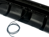 Black bumper with visible wiring extending from it, placed on a smooth white surface, partially covered by a coiled black cable with exposed colored wires.