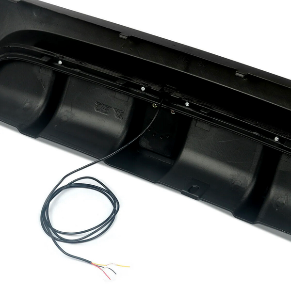 Black bumper with visible wiring extending from it, placed on a smooth white surface, partially covered by a coiled black cable with exposed colored wires.