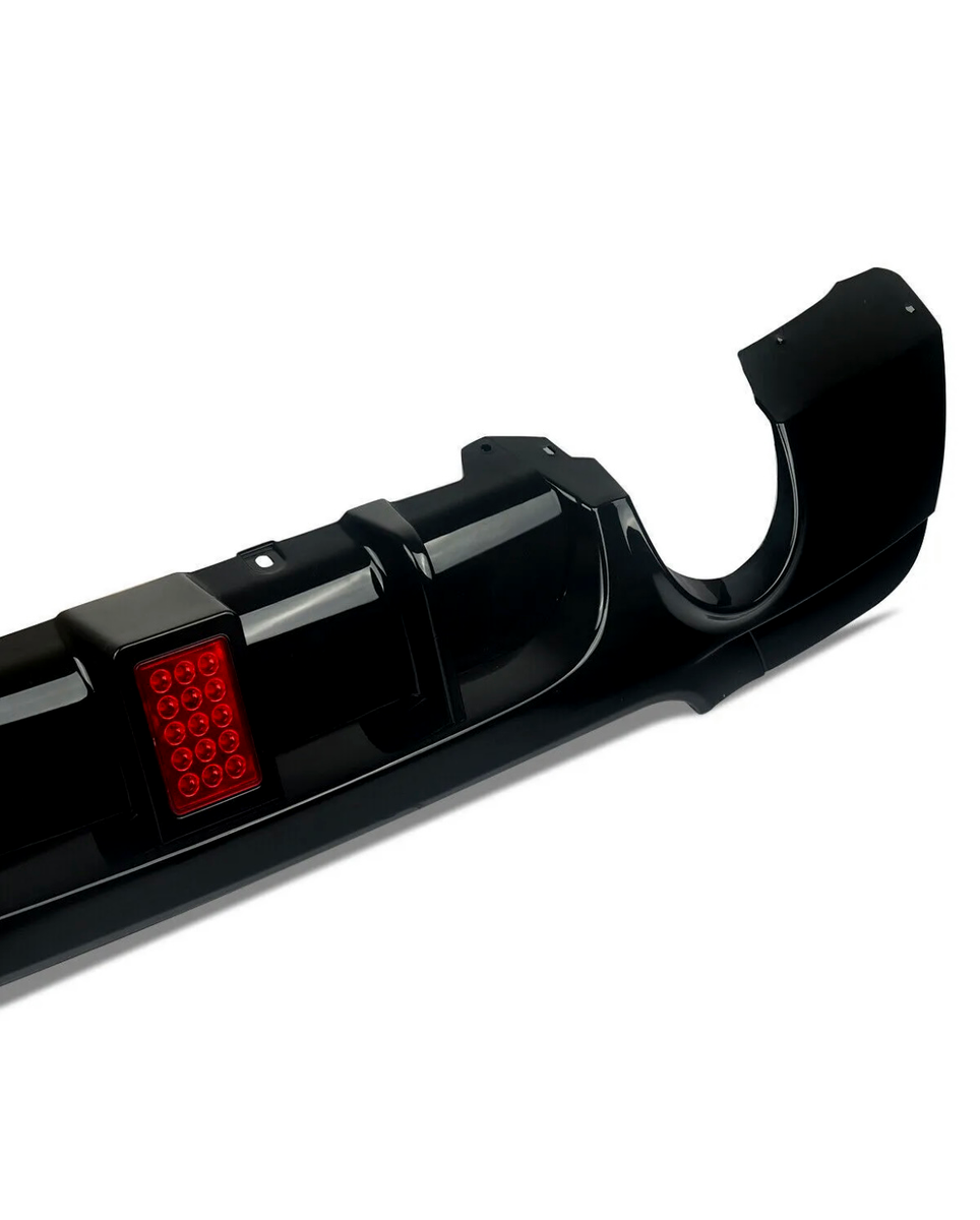 Black car rear bumper, featuring a red reflective square panel, lies on a plain white background. The bumper has smooth curves and defined edges, with openings for exhaust pipes.