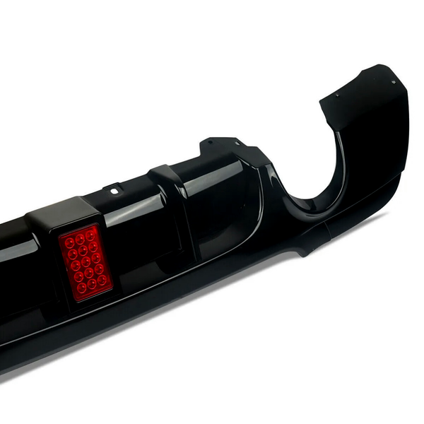 Black car rear bumper, featuring a red reflective square panel, lies on a plain white background. The bumper has smooth curves and defined edges, with openings for exhaust pipes.