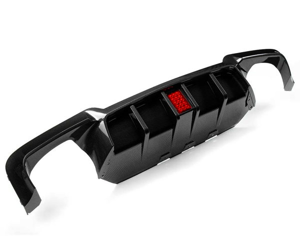 A carbon fiber car diffuser with a central red reflector. It features fins for aerodynamic purposes and is set against a plain white background, highlighting its sleek design.