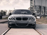 A gray BMW car stands still, positioned on train tracks. In the background, large industrial silos rise against a cloudy sky.