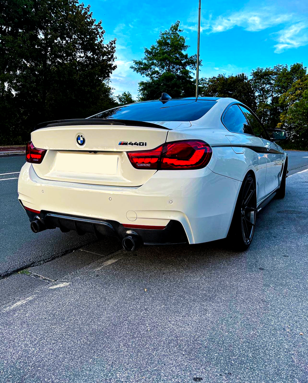 A white BMW M440i car is parked on a street, surrounded by trees under a clear blue sky.