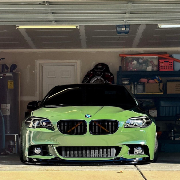 A sleek green car is parked in a cluttered garage, surrounded by shelves filled with boxes and various household items.