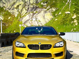 A yellow BMW sports car is parked on a stone road, with a mountainous landscape featuring green vegetation and rocky cliffs in the background.