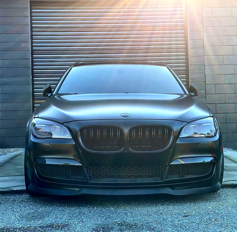 A sleek, black car is parked in front of a closed, metallic garage door on a sunny day, with sunlight casting rays across the scene.