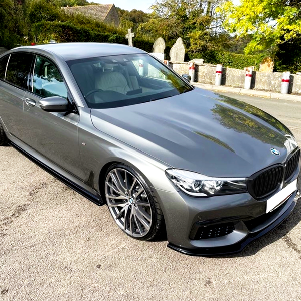 A sleek, grey sedan is parked on a quiet road beside stone markers and lush greenery, under a clear sky.