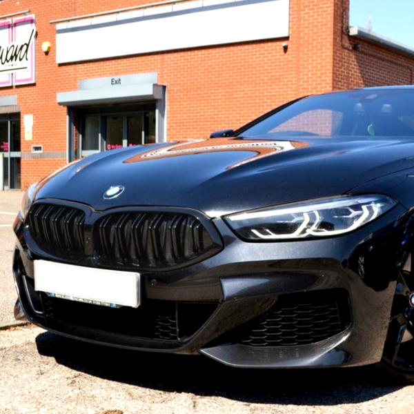 A black BMW car is parked in front of a building with a brick exterior. Visible signs read "Exit" and partially visible pink sign "Brand."