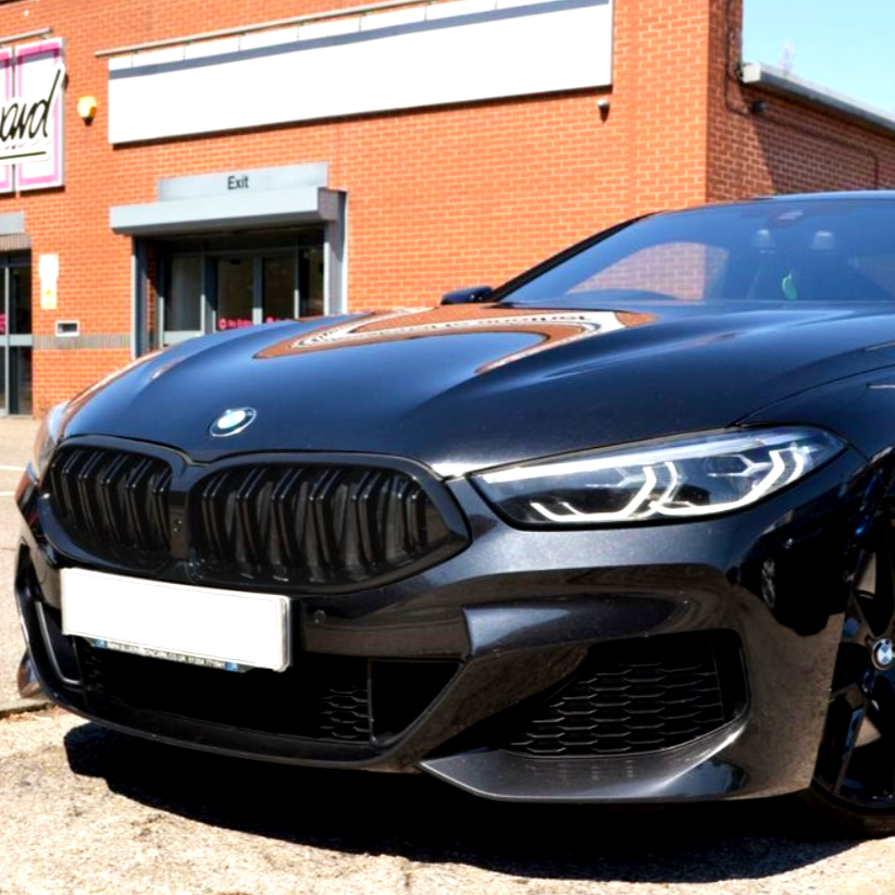 A sleek, dark-colored BMW car is parked in front of a brick building. The building has a sign reading "Exit" above a doorway, with another sign partially visible.