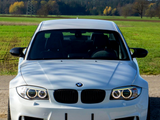 A white BMW car is parked on a rural road. It is facing forward with a power line in the background and surrounded by green fields and distant trees.