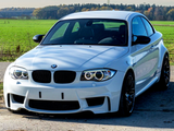 A white sports car is parked on a rural road with green fields and trees in the background under a clear sky.