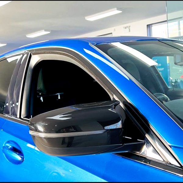 A blue car parked indoors, with its window slightly open and a visible side mirror reflecting the ceiling lights. The environment is a well-lit showroom with visible signage.