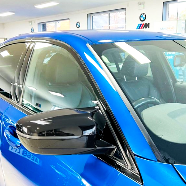 A shiny blue car is parked in a well-lit showroom, surrounded by other vehicles. Visible text includes “Your Next Car” and “MotoNovo,” indicating a promotional setting.