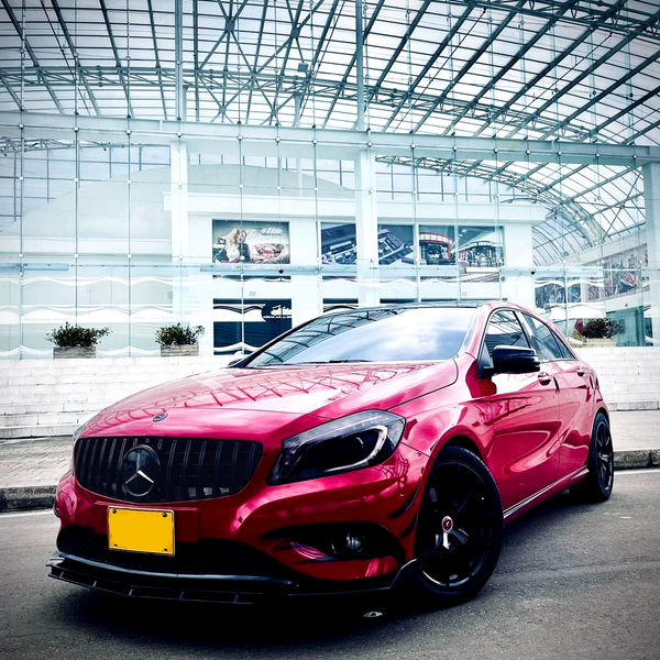 A red car with a distinctive emblem is parked on a street. It appears sleek and polished, in front of a modern glass building with a translucent roof structure.