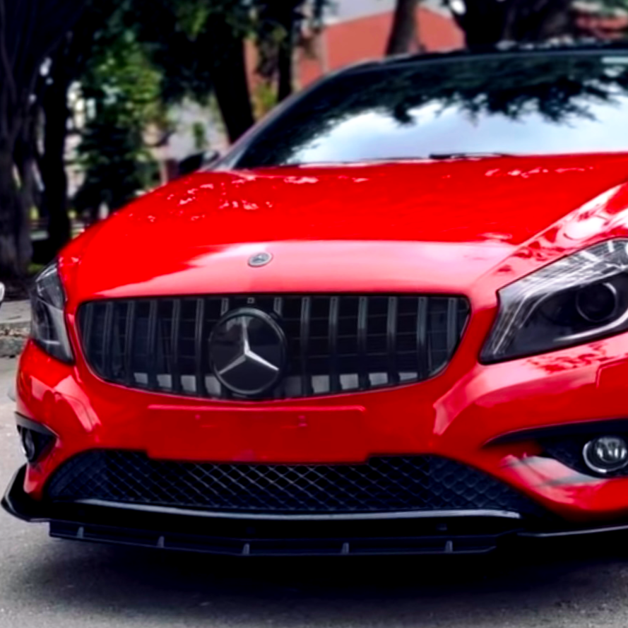 Red sports car with a prominent Mercedes-Benz logo on the grill, parked on a street lined with trees and buildings.