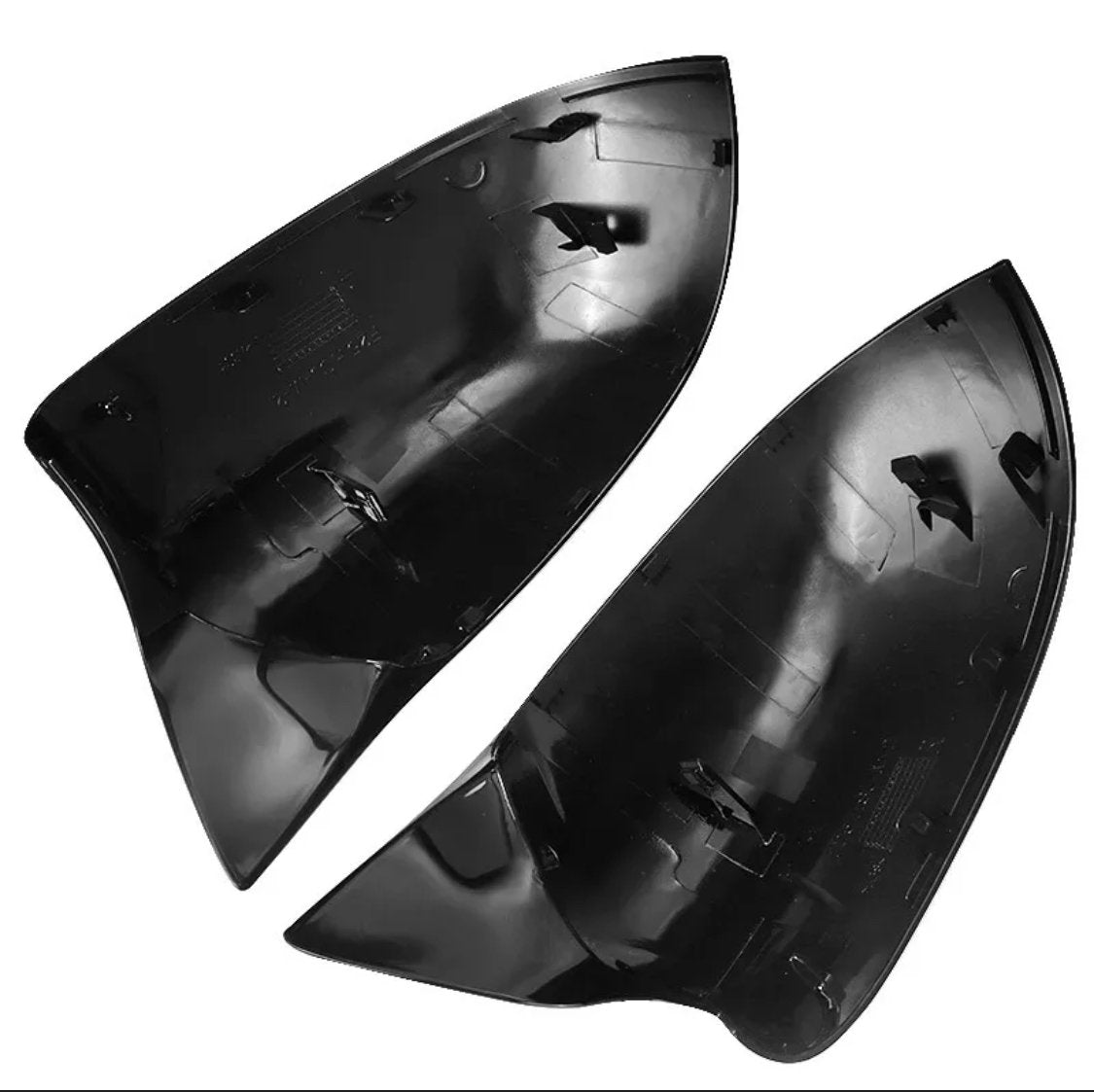 Two black, glossy, shark-fin shaped objects lie side by side, showcasing internal clips and connectors. They appear to be vehicle parts, possibly mirror covers, set against a plain white background.