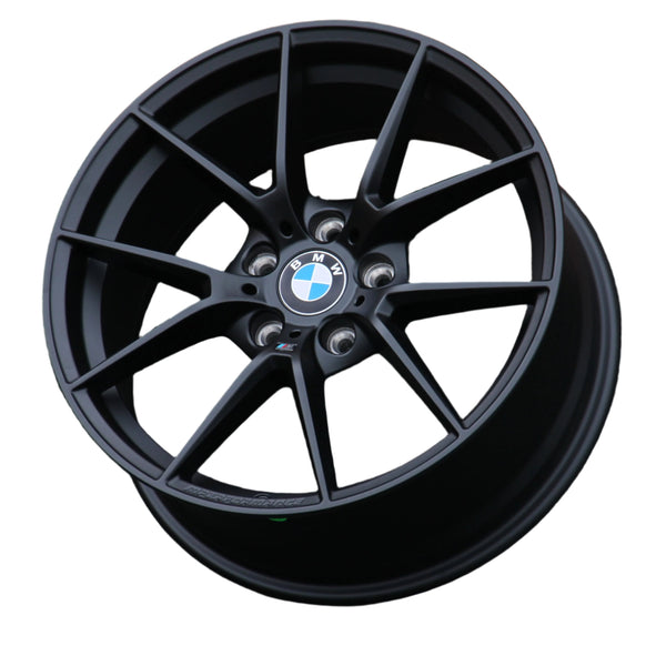 A black, multi-spoke BMW wheel rim with visible lug holes and a "BMW" center cap, displayed against a plain white background. Text on the rim reads "M Performance."