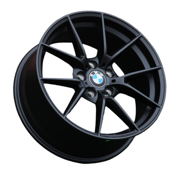 A black BMW alloy wheel with a multi-spoke design is positioned against a white background. The BMW logo is centered, surrounded by lug nut holes. "M PERFORMANCE" text is embossed on the rim.