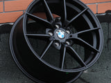 A black BMW car wheel rests against a brick wall. The wheel features multiple spokes and a BMW logo at its center. A small 