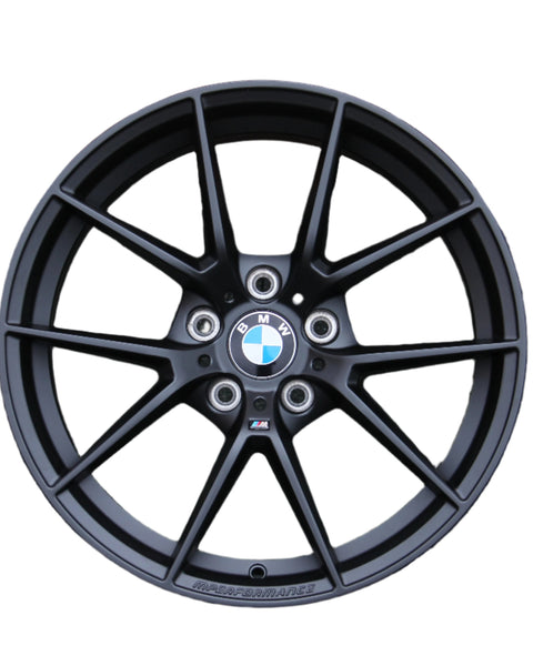 A black BMW car wheel rim with a multi-spoke design showcases the BMW logo at the center. Text includes "BMW" and "M PERFORMANCE." The background is plain white.