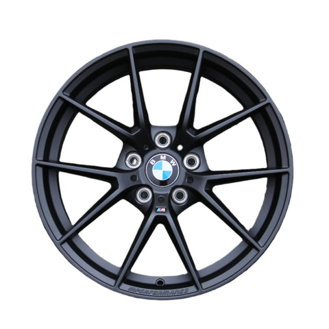A black BMW car wheel rim with a multi-spoke design showcases the BMW logo at the center. Text includes "BMW" and "M PERFORMANCE." The background is plain white.