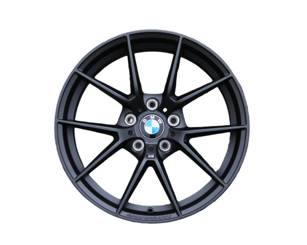 A black alloy wheel displaying the BMW logo is positioned centrally. Text "M PERFORMANCE" is etched on the rim. The wheel spokes radiate outward, isolated on a plain white background.