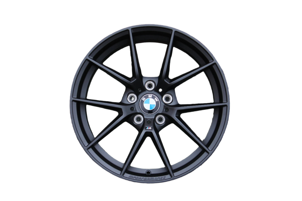 A black alloy wheel displaying the BMW logo is positioned centrally. Text "M PERFORMANCE" is etched on the rim. The wheel spokes radiate outward, isolated on a plain white background.