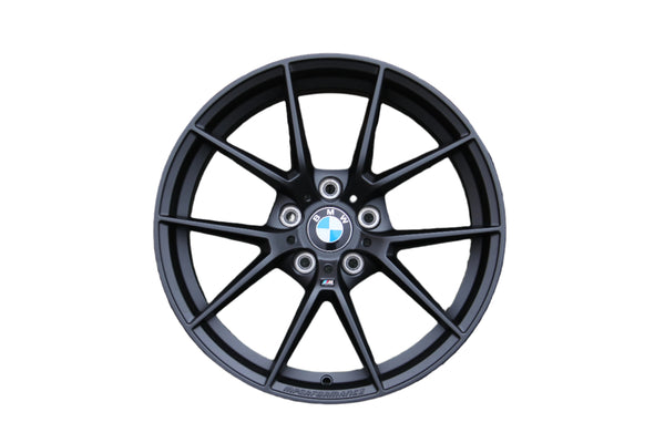 A black alloy wheel displaying the BMW logo is positioned centrally. Text "M PERFORMANCE" is etched on the rim. The wheel spokes radiate outward, isolated on a plain white background.
