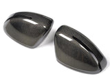 Two black carbon fiber car mirror covers with a sleek, glossy finish, positioned side by side, against a plain white background.