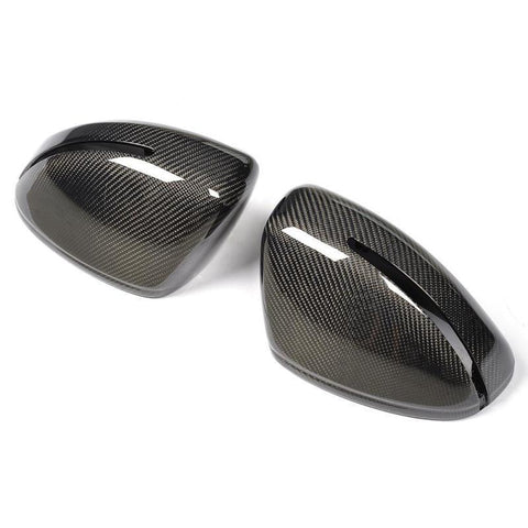 Two carbon fiber car side mirror covers rest on a white surface, displaying a glossy, woven texture with elongated openings near the edges, reflecting light.
