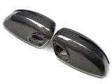 Two glossy carbon fiber side mirror covers rest on a white background, showcasing a sleek, modern design with visible weave patterns and mounting holes.