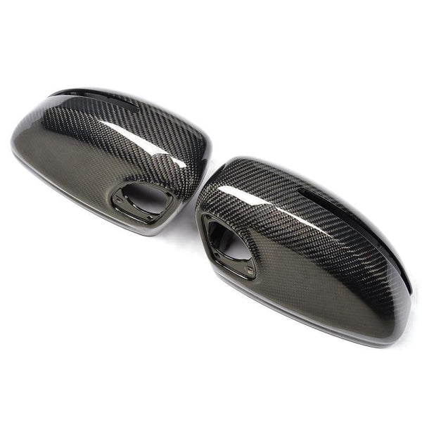 Two glossy carbon fiber side mirror covers rest on a white background, showcasing a sleek, modern design with visible weave patterns and mounting holes.