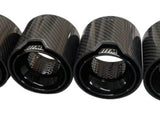 Four carbon-fiber exhaust tips display a glossy finish and perforated interiors. They are aligned horizontally on a plain, white background. Each tip has 
