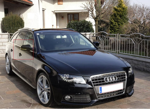 A black Audi station wagon is parked on a stone driveway in front of a house with a garden. The car's front grille and silver wheels are visible.