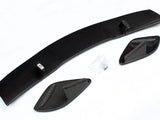 Carbon fiber car spoiler components lie on a white surface, consisting of a long curved piece and two smaller side elements. A small bag containing screws is nearby.