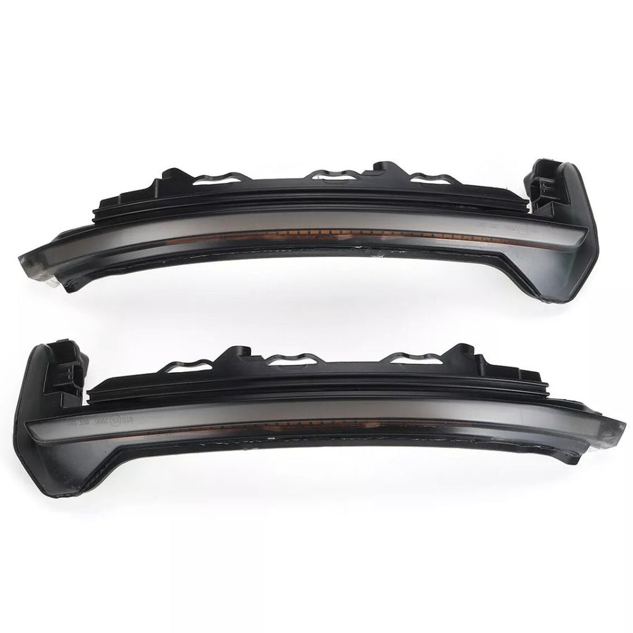 Two dark, curved car headlight components with intricate detailing are aligned horizontally on a plain white background, showing side profiles and a curved design for vehicle integration.