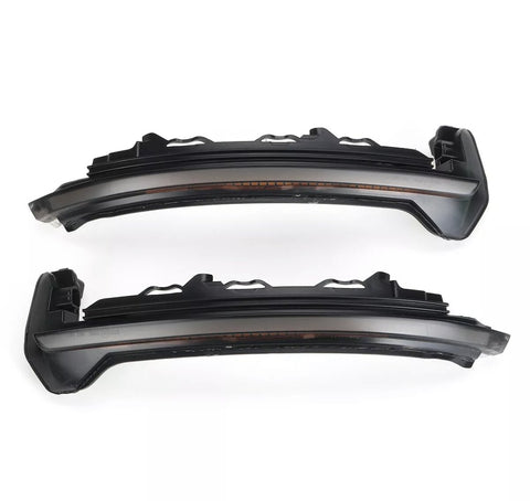 Two dark, curved car headlight components with intricate detailing are aligned horizontally on a plain white background, showing side profiles and a curved design for vehicle integration.