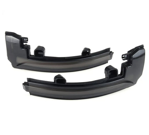 Two black plastic automotive light covers lie side by side, appearing glossy and curved, intended for vehicle use in a neutral, light-colored space.