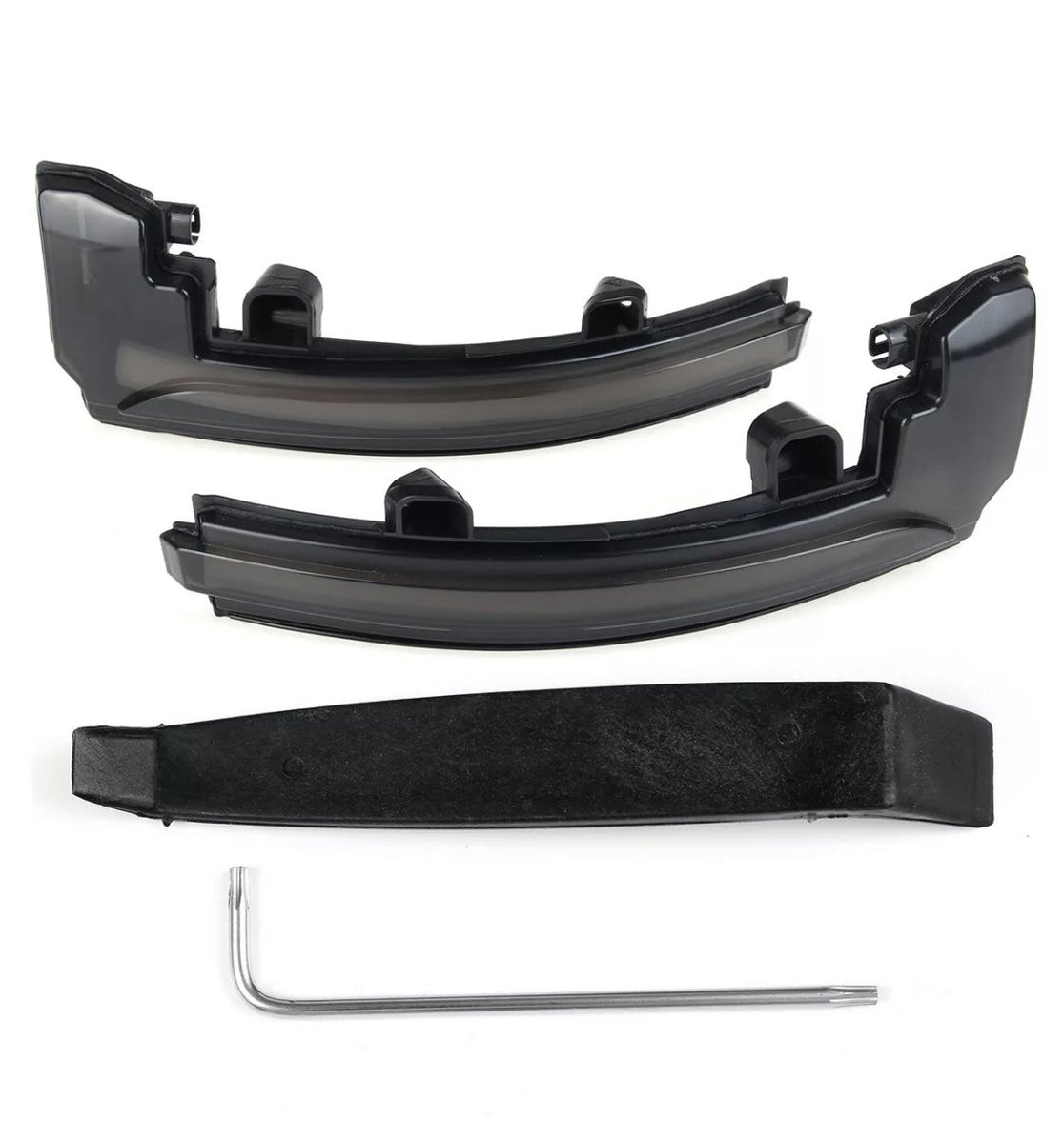 Two black plastic car light cover pieces rest on a white surface, accompanied by a black mounting bracket and a silver L-shaped tool beneath them.