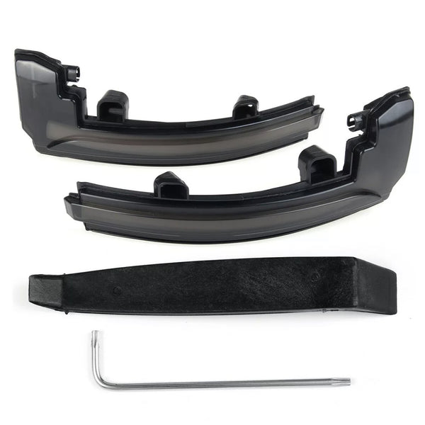 Two black plastic car light cover pieces rest on a white surface, accompanied by a black mounting bracket and a silver L-shaped tool beneath them.