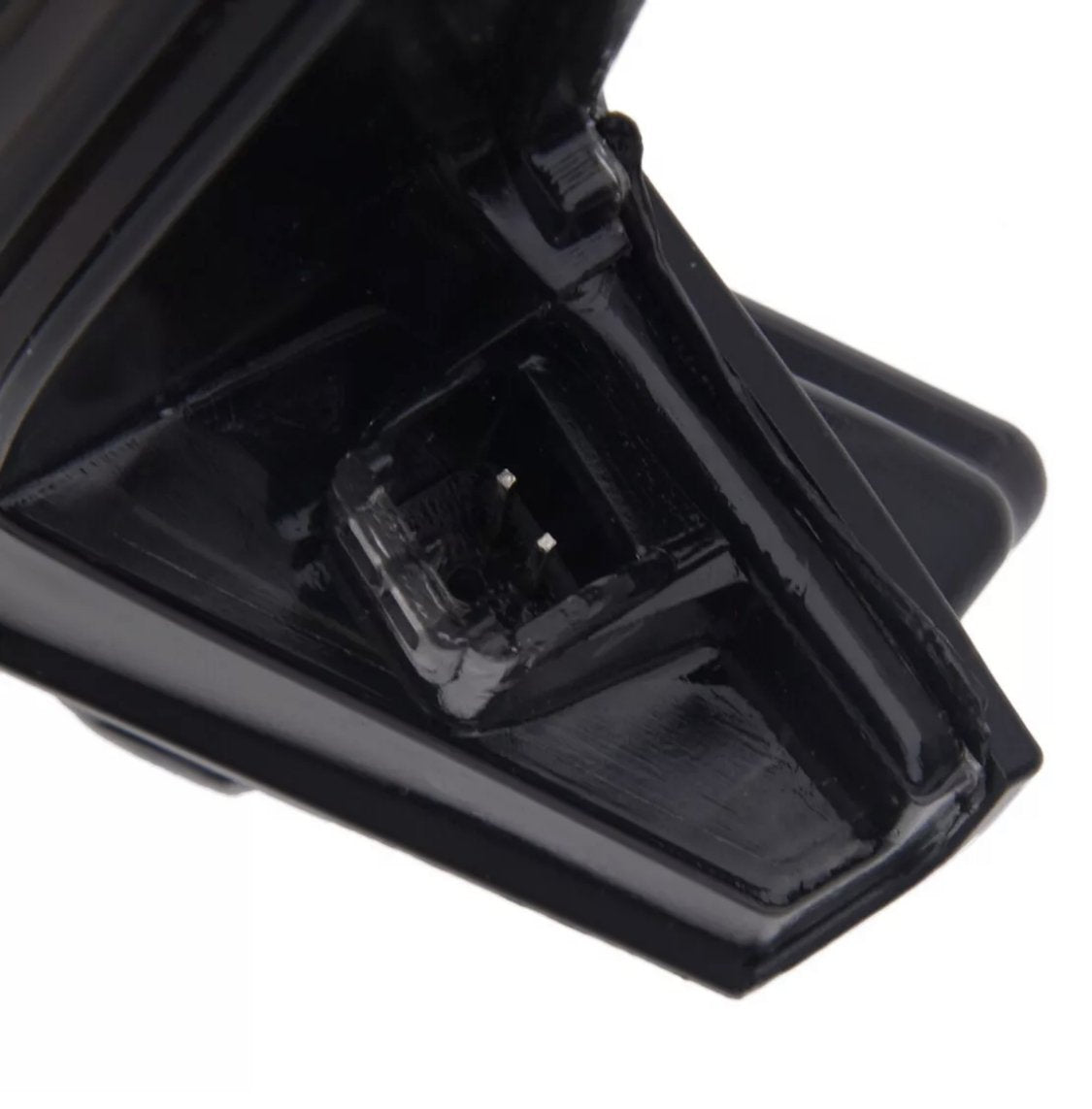 A black plastic part with a small square depression containing metal prongs, possibly for electrical connection, is shown against a plain background.
