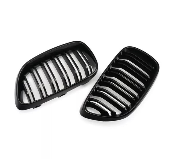 Two black, kidney-shaped car grilles with vertical slats lie on a white background, suggesting automotive parts likely used for air intake and vehicle front decoration.